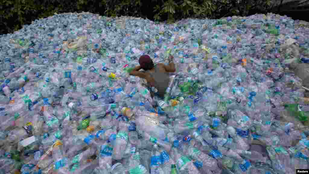 Seorang pekerja menggunakan tali untuk menarik botol-botol plastik di pusat daur ulang di Mumbai, India.