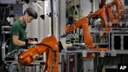 FILE - In this Aug. 21, 2015 photo, a Chinese man works amid orange robot arms at Rapoo Technology factory in southern Chinese industrial boomtown of Shenzhen. 