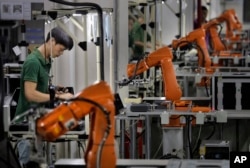 FILE - In this Aug. 21, 2015 photo, a Chinese man works amid orange robot arms at Rapoo Technology factory in southern Chinese industrial boomtown of Shenzhen.