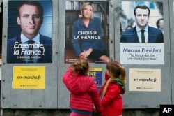 Children walk past election campaign posters for French centrist presidential candidate Emmanuel Macron and far-right candidate Marine Le Pen, in Osses, southwestern France, May 5, 2017. France is voting Sunday in the second round of the presidential elec