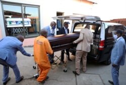 Des employés de Sopema Funerals placent le corps d'une personne décédée dans un corbillard à Soweto, au sud-ouest de Johannesburg, en Afrique du Sud, le 4 août 2020.