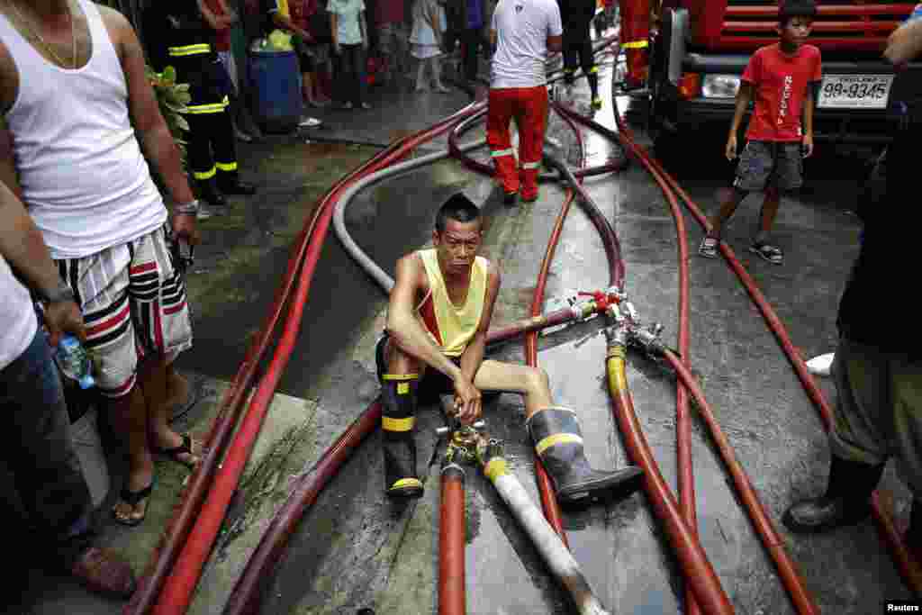 A man operates hoses as firefighters try to put out a fire in Bangkok's Sukhumvit area, Thailand. Dozens of houses were destroyed after a fire broke out in the residential area in central Bangkok.