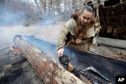 Mashpee Wampanoag Phillip Wynne pours water to control fire and temperatures while making a boat, from a tree at the Wampanoag Homesite at Plimoth Plantation, in Plymouth, Mass.