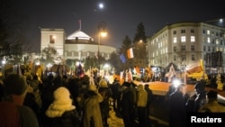 FILE - Demonstrators wave Polish and European Union flags during a protest outside the Parliament building in Warsaw, Jan. 11, 2017.