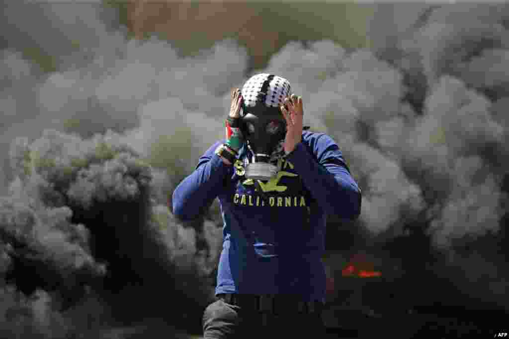 A Palestinian man wears a gas mask next to burning tires during a protest in the West Bank city of Ramallah.