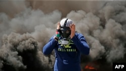 A Palestinian man wears a gas mask next to burning tires during a protest in the West Bank city of Ramallah, April 6, 2018.