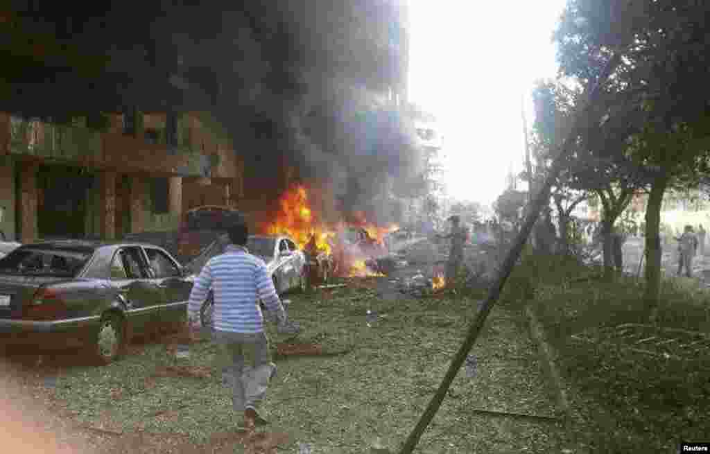 A man walks near burning cars at the site of explosions near the Iranian embassy in Beirut, Nov 19, 2013. 