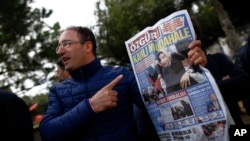 FILE - A man shows the front page of the daily Ozgur with a headline that reads " bloody intervention" as people gather outside the headquarters of Zaman newspaper in Istanbul, March 6, 2016. 