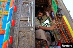 A driver holds open the door of the carved wood cab of his decorated truck in Faisalabad, Pakistan, May 4, 2017.