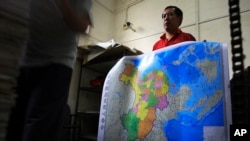 FILE - A worker holds a new officially approved map of China that includes the islands and maritime area that Beijing claims in the South China Sea, at a printing factory in Changsha in south China's Hunan province.