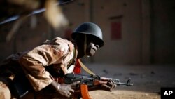 FILE - A Malian soldier takes cover behind a truck during exchanges of fire with jihadists in Gao, northern Mali, Feb. 10, 2013.