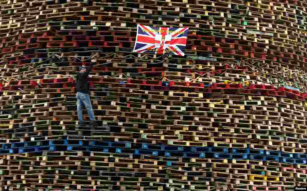 A man gestures as he climbs wood stacked for a bonfire on the Shankill Road in West Belfast, Northern Ireland.