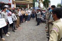 Supporters of Rong Chhun, leader of the Cambodian Confederation of Unions hold placards as local security personnel guard during a protest in front of Phnom Penh municipal court on August 1, 2020. Cambodia police have arrested Rong Chhun, a prominent union leader for alleged incitement over the country's disputed border with Vietnam, they said August 1, the latest crackdown against opposition voices in the kingdom. (Photo by TANG CHHIN Sothy/AFP)