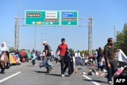 Migrants and refugees walk around tents as they wait after Turkish police forces block them on a highway near Edirn during their march to the border between Turkey and Greece on Sept. 19, 2015.