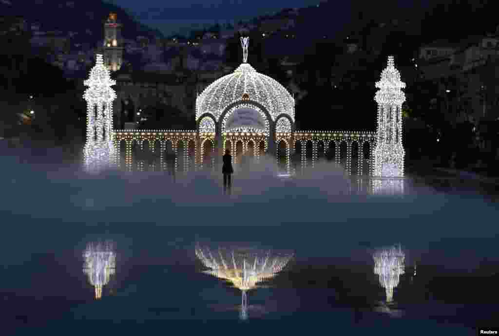 People stand in the mist as they look at a replica of the casino along the Promenade jetty as part of the Christmas holiday illuminations in Nice, France.