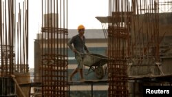 FILE - A worker pushes a wheelbarrow to collect cement at a construction site of a residential building in Mumbai, India, Aug. 31, 2018.