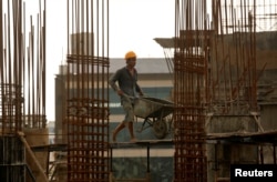 FILE - A worker pushes a wheelbarrow to collect cement at a construction site of a residential building in Mumbai, India, Aug. 31, 2018.
