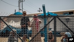 Mideast Iraq Faltering IS: In this August 17, 2016 photo, men wait behind a fenced area where they are interrogated before being allowed to stay, at the Dibaga Camp for displaced people, in Hajj Ali, northern Iraq.