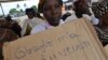 A victim of the 2010 post-election crisis hold a placard reading "Gbagbo turned me into a widow" during a gathering in the Kouassai popular district of Abidjan, Feb. 28, 2013. 