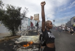 In this Saturday, May 30, 2020 file photo, a protester poses for photos next to a burning police vehicle in Los Angeles during a demonstration over the death of George Floyd. a black man who was killed in police custody in Minneapolis on May 25.