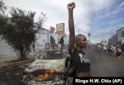 In this Saturday, May 30, 2020 file photo, a protester poses for photos next to a burning police vehicle in Los Angeles during a demonstration over the death of George Floyd. a black man who was killed in police custody in Minneapolis on May 25.