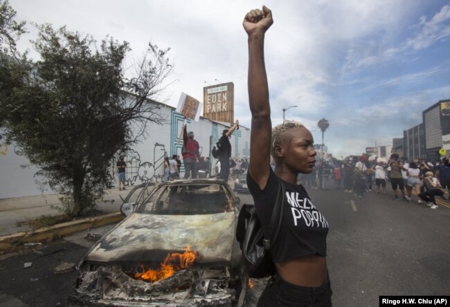 Seorang pemrotes berpose untuk foto-foto di sebelah kendaraan polisi yang terbakar di Los Angeles selama demonstrasi atas kematian George Floyd. seorang pria kulit hitam yang terbunuh dalam tahanan polisi di Minneapolis, 30 Mei 2020. (Foto: AP/Ringo H.W. Chiu)