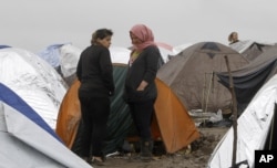 Syrian refugee women look on, standing in the mud between tents in an improvised camp on the border line between Macedonia and Serbia near the northern Macedonian village of Tabanovce, March 11, 2016.