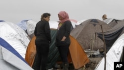 Syrian refugee women look on, standing in the mud between tents in an improvised camp on the border line between Macedonia and Serbia near the northern Macedonian village of Tabanovce, March 11, 2016. 