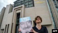 FILE - A journalist poses with a portrait of Turkish journalist Ahmet Altan, June 19, 2017, in front of the Istanbul courthouse. 