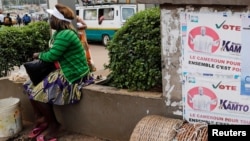 FILE - A street vendor sits near placards of presidential candidates Cabral Libii (R) of Univers party and Maurice Kamto of the Movement for Renaissance, in Yaounde, Cameroon, Oct. 5, 2018.