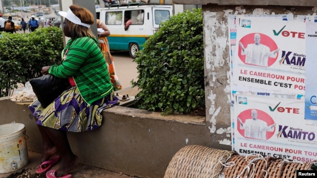 FILE - A street vendor sits near placards of presidential candidates Cabral Libii (R) of Univers party and Maurice Kamto of the Movement for Renaissance, in Yaounde, Cameroon, Oct. 5, 2018.