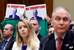 Protesters hold up signs and shirts behind Environmental Protection Agency Administrator Scott Pruitt, accompanied by Holly Greaves, EPA chief financial officer, as they testify during a hearing of the House Energy and Commerce subcommittee on Capitol Hill in Washington, April 26, 2018.
