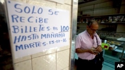 A man counts his 100-bolivar notes next to a sign alerting customers with a message in Spanish that reads: ”100-bolivar notes will only be received until Tuesday, 12-13-16,” inside a bakery in downtown Caracas, Venezuela, Dec. 12, 2016. 