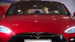 FILE - A man sits behind the steering wheel of a Tesla Model S electric car on display at the Beijing International Automotive Exhibition in Beijing, April 25, 2016.