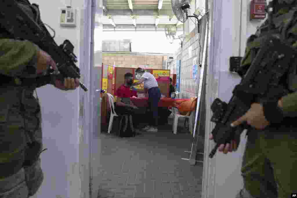Israeli soldiers stand guard as a Palestinian who works in Israel receives a Moderna COVID-19 vaccine at the Tarkumiya crossing between the West Bank and Israel.
