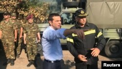 FILE - Greek Prime Minister Alexis Tsipras speaks with a firefighter officer as he visits the village of Mati, following a wildfire near Athens, Greece, July 30, 2018.