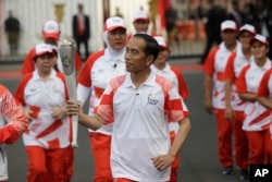 FILE - Indonesian President Joko "Jokowi" Widodo, center, holds the Asian Games torch as he runs during an independence day ceremony at Merdeka Palace in Jakarta, Indonesia, Aug. 17, 2018.