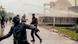In this file photo, hooded violent demonstrators hurl rocks towards police water cannons behind the security fence surrounding the nuclear power plant in Brokdorf, Germany, on June 7, 1986. (AP Photo/Heribert Proepper, file)