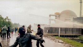 In this file photo, hooded violent demonstrators hurl rocks towards police water cannons behind the security fence surrounding the nuclear power plant in Brokdorf, Germany, on June 7, 1986. (AP Photo/Heribert Proepper, file)