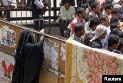 A woman takes photos of men from behind a barrier at Taghyeer (Change) Square where anti-government protesters have been camping for more than a year to demand regime change in Sanaa, April 10, 2012.