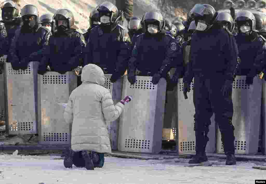 Một phụ nữ quỳ xuống khẩn cầu cảnh sát Ukraina tại địa điểm xảy ra đụng độ với người biểu tình chống chính phủ ở Kyiv. Người biểu tình dựng lên nhiều rào chắn đường và chiếm đóng một tòa nhà cấp bộ của chính phủ hôm thứ Sáu sau khi đàm phán khủng hoảng thất bại.