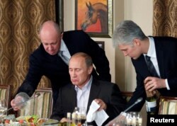 FILE - Evgeny Prigozhin, left, assists then-Russian Prime Minister Vladimir Putin during a dinner with foreign scholars and journalists at the restaurant Cheval Blanc outside Moscow, Nov. 11, 2011.