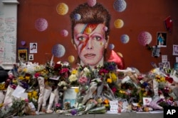 Tributes lie placed around a mural of British singer David Bowie by artist Jimmy C in Brixton, south London, Thursday, Jan. 14, 2016.