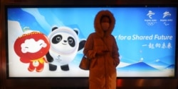 A woman waits on a bus station in front of an advertising board featuring Bing Dwen Dwen, the Beijing 2022 Winter Olympic Mascot and Shuey Rhon Rhon, the 2022 Beijing Winter Paralympic Games Mascot, in Beijing on January 19, 2022. (Fabrizio Bensch/Reuters)