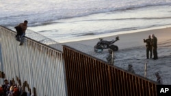 15일 중남미 출신 이민자 행렬 캐러번이 미국과 멕시코 국경에 도착한 가운데, 한 이민자가 국경담장에 올라타자 미국 국경수비대가 그 모습을 지켜보고 있다. 