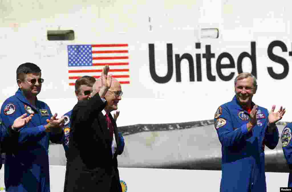 Former U.S. Senator and astronaut John Glenn (C) waves to the crowd at the National Air and Space Museum's Udvar-Hazy Center for the arrival of space shuttle Discovery (back) while former shuttle commanders applaud in Virginia, April 19, 2012. 