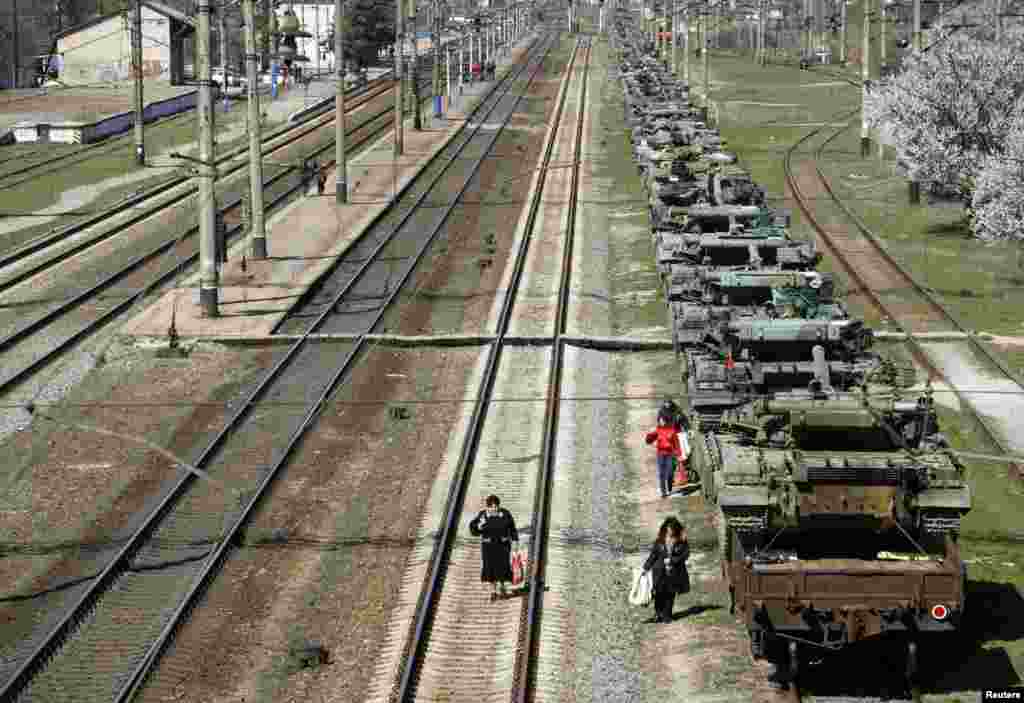 Commuters walk along railway lines next to Ukrainian tanks ready to depart from Crimea near Simferopol, March 31, 2014.