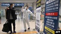 30일 한국 인천국제공항에서 방역복을 입은 관계자가 입국장에 도착한 여행객에게 신종 코로나 방역 조치를 안내하고 있다.