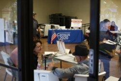In this Feb. 8, 2020, photo, people volunteer to get people registered to vote and a booth offering employment for the upcoming 2020 census stands in the background, during the celebration of the town's 45th year since it was incorporated, in Guadalupe, A