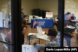 In this Feb. 8, 2020, photo, people volunteer to get people registered to vote and a booth offering employment for the upcoming 2020 census stands in the background, during the celebration of the town's 45th year since it was incorporated, in Guadalupe, A